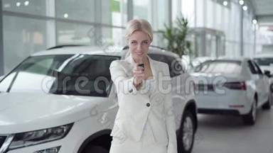 自信的年轻金发女人在镜头前拿出汽车钥匙，微笑着。 穿白色西装的女商人<strong>买</strong>车